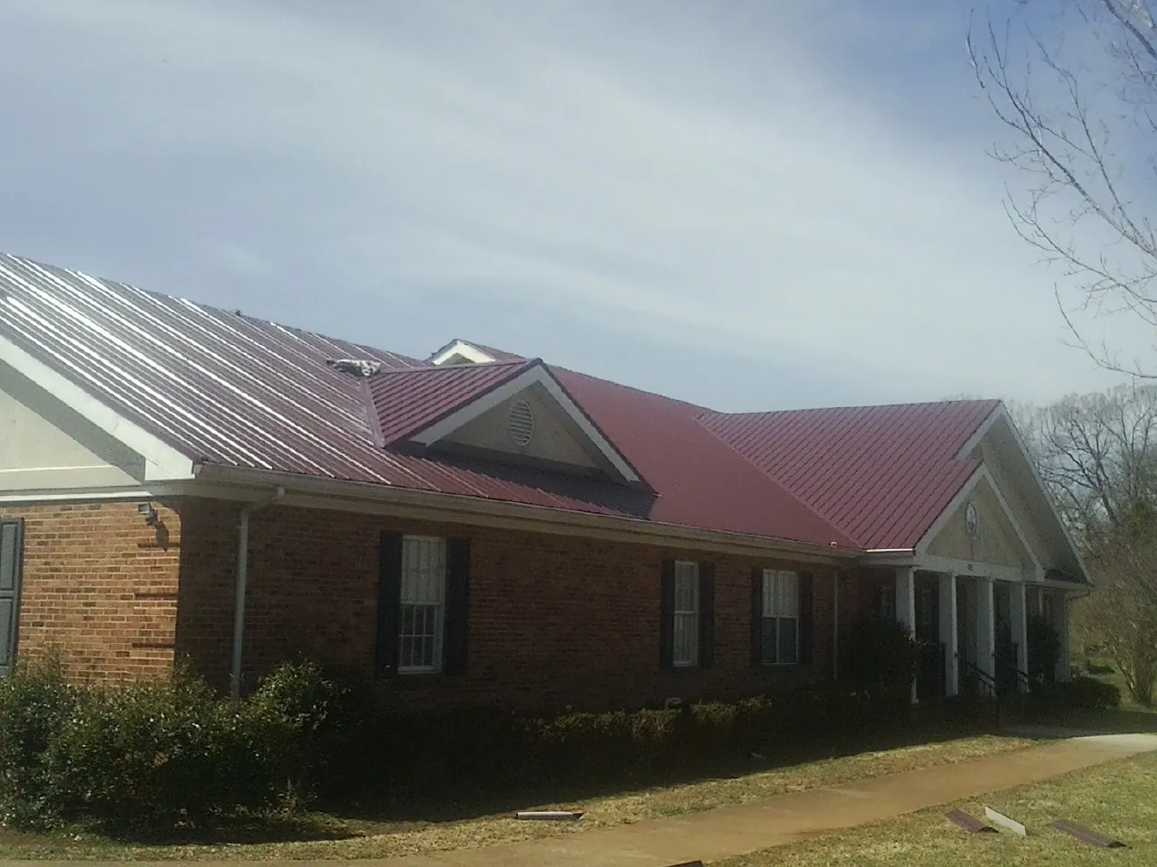 Red metal roof with gabled entries on a long brick building, from a Hail Damage Roof Repair job in Nicasio