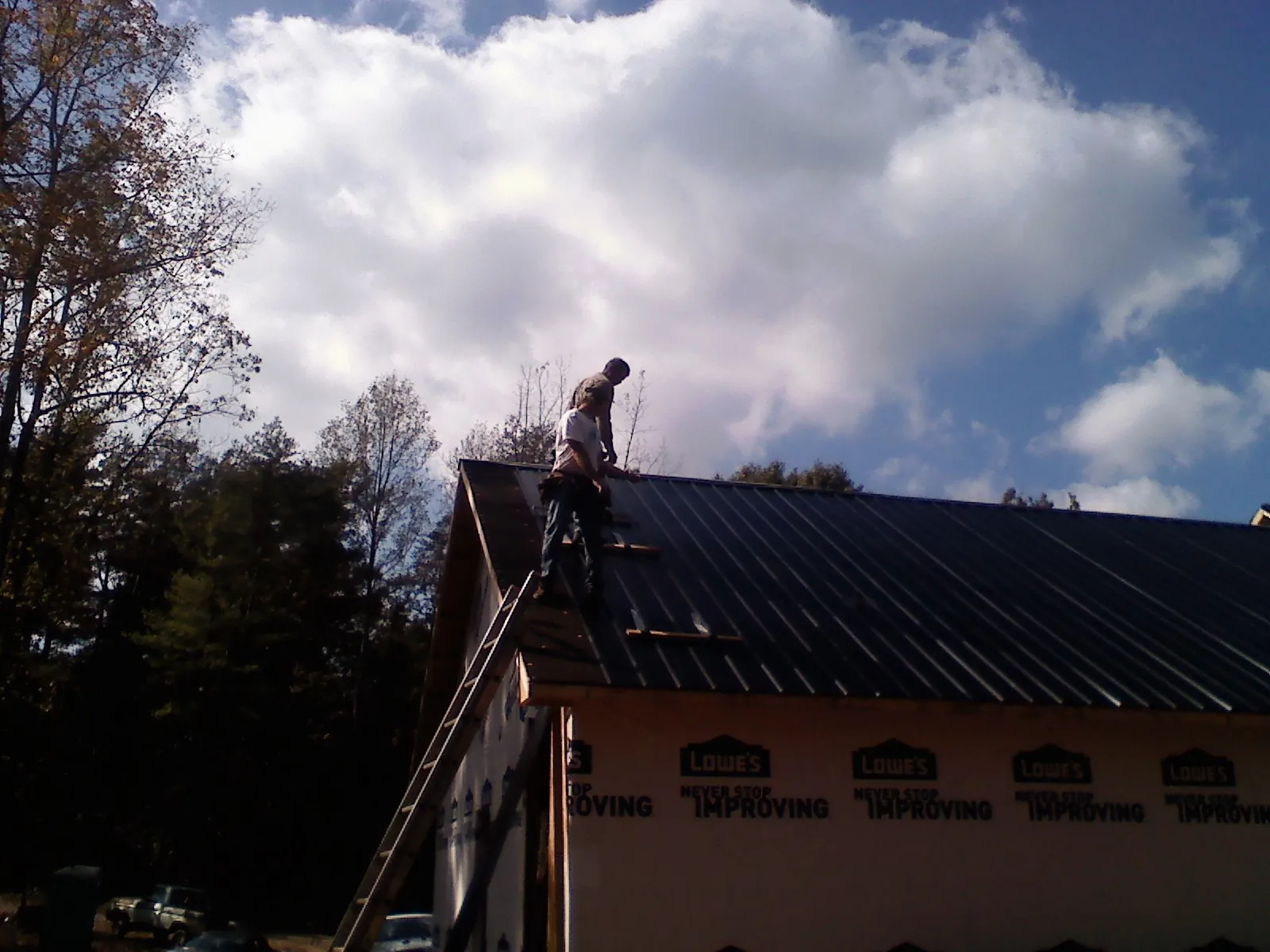 Roofer fastening dark metal panels high against a cloudy sky, from a Roof Inspection job in Nicasio